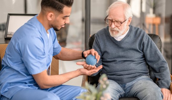 Pfleger behandelt älteren Palliativpatienten mit Massageball