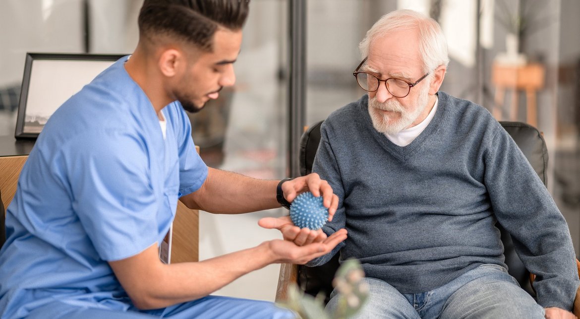 Pfleger behandelt älteren Palliativpatienten mit Massageball