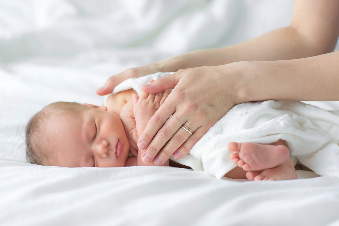 Baby liegt mit dem Bauch auf Decke zwei Hände liegen auf dem Rücken des Babys