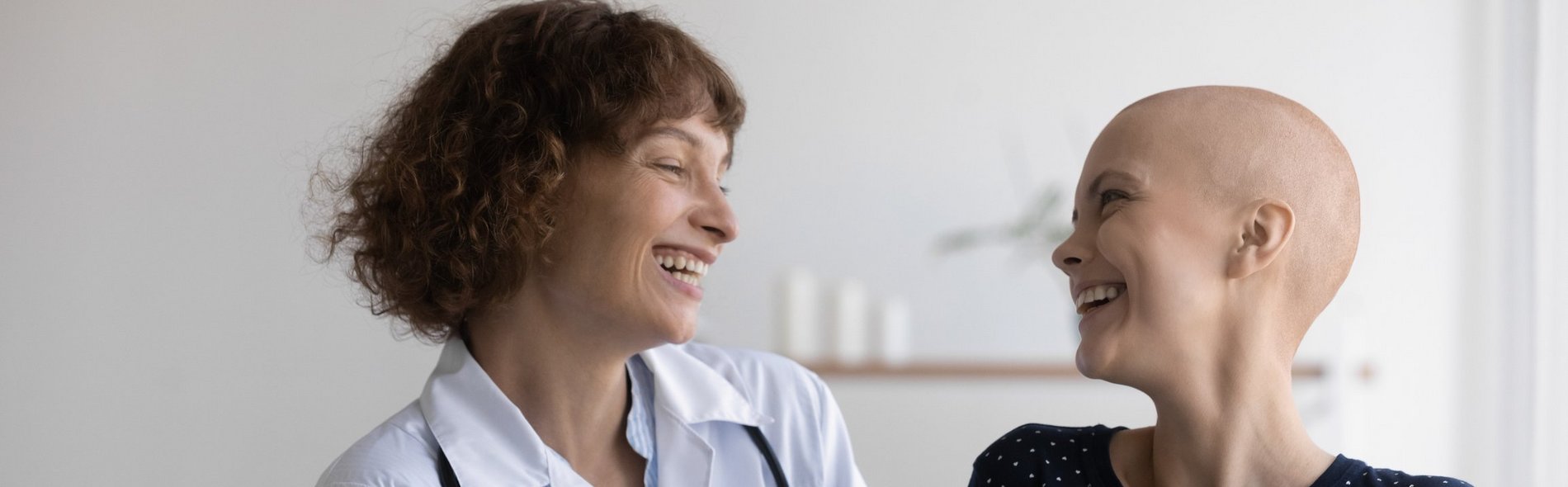 Eine junge Patientin ohne Haare und eine Ärztin lachen zusammen