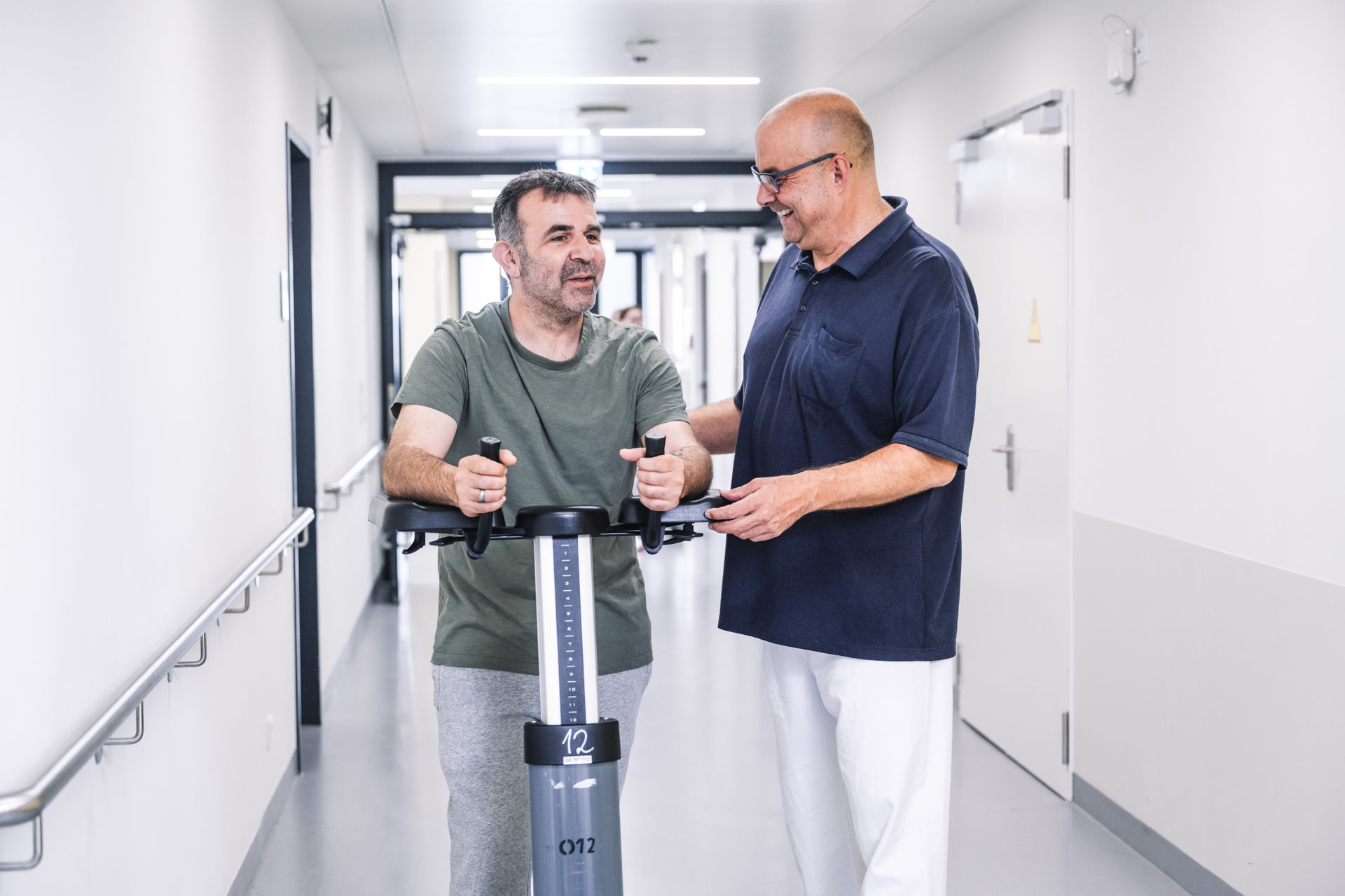 Physiotherapie am Patienten mit Gehilfe auf dem Stationsflur