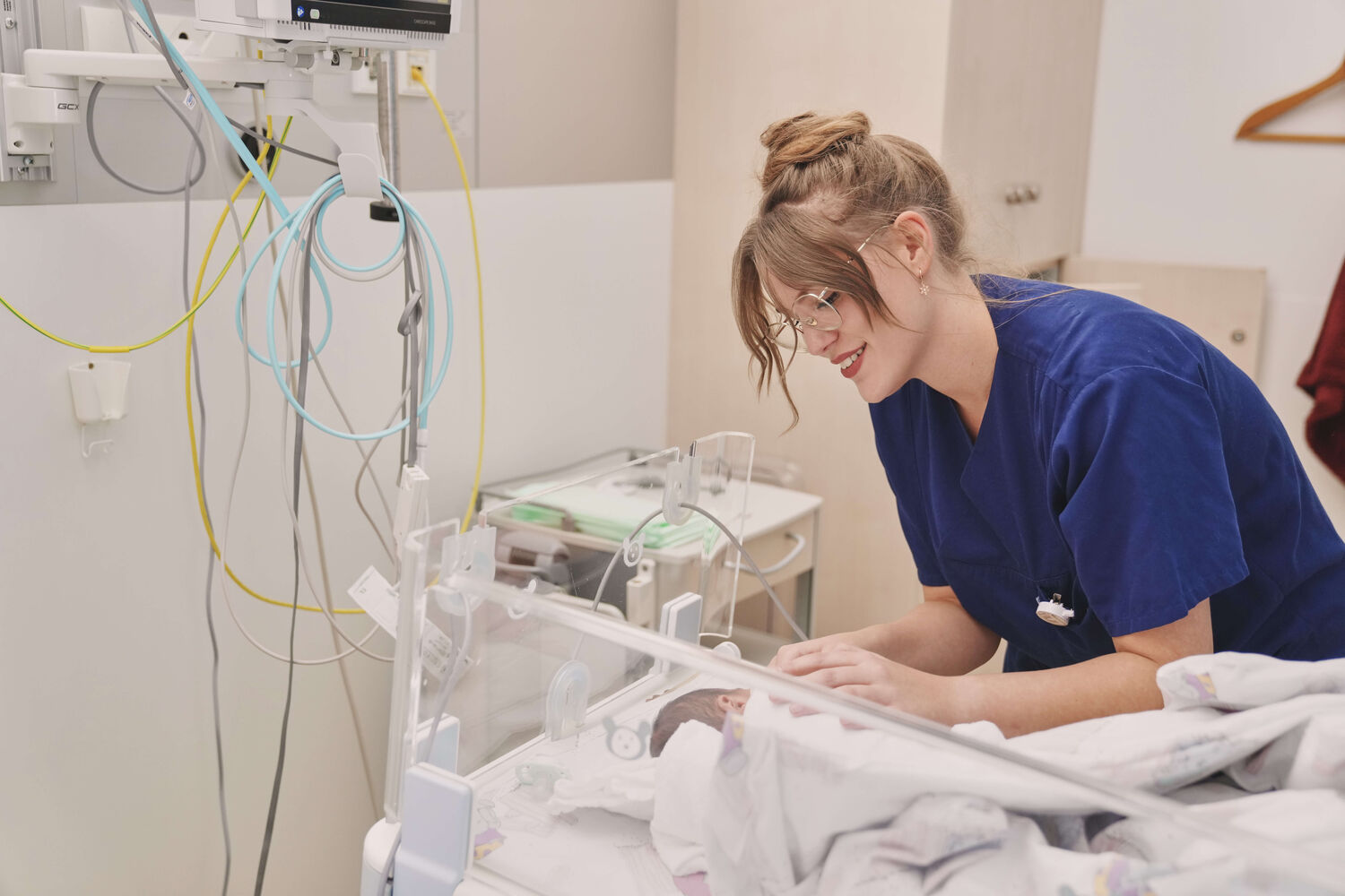 Das Bild zeigt eine Kinderkrankenpflegerin, welche die Vitalwerte eines Neugeborenen prüft.