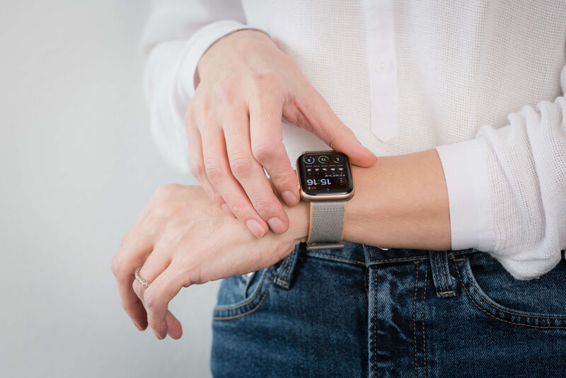 Eine Frau in einem weißen Hemd und Jeans hält ihre Apple Watch.