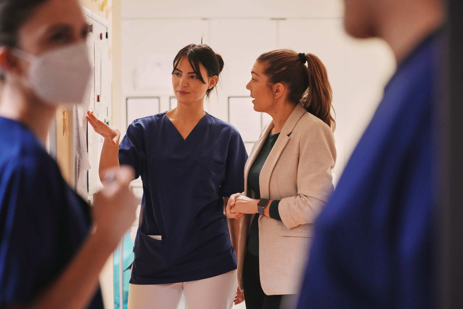 Eine Gruppe von Krankenschwestern unterhält sich miteinander. Sie stehen in einem Raum mit medizinischer Ausrüstung.