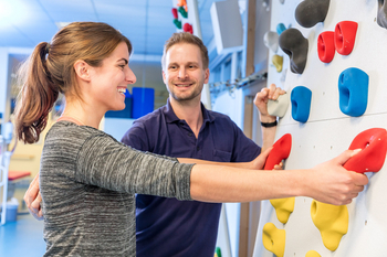 Therapeut mit Patientin an einer Kletterwand