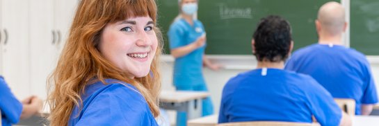 eilnehmer in blauen Outfits folgen einer Schulung über medizinische Themen.