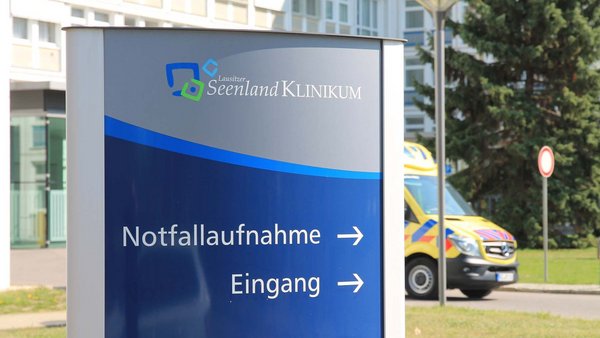 Rettungswagen fährt hinter Wegweiser zur Notfallaufnahme