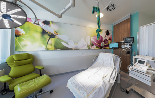 Kreißsaal mit Liege und grünem Sessel und medizinischen Geräten