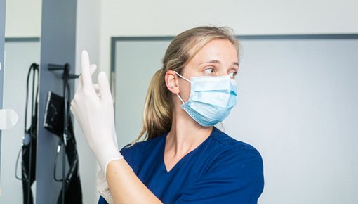 Foto einer Pflegekraft, die sich Gummihandschuhe anzieht. 