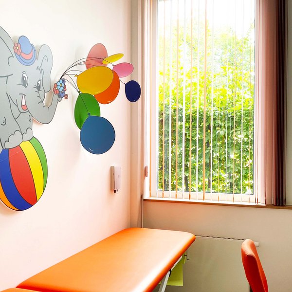 Behandlungszimmer mit Behandlungsliege und bunter Wandapplikation für eine freundliche Umgebung.
