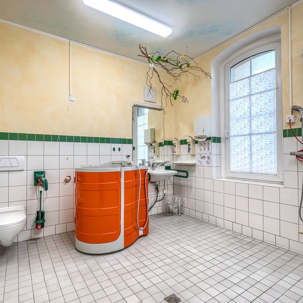 Barrierefreies Badezimmer mit einer orangen Sitzbadewanne, schwellenloser Dusche und sicherheitsfördernden Elementen wie Haltegriffen.  