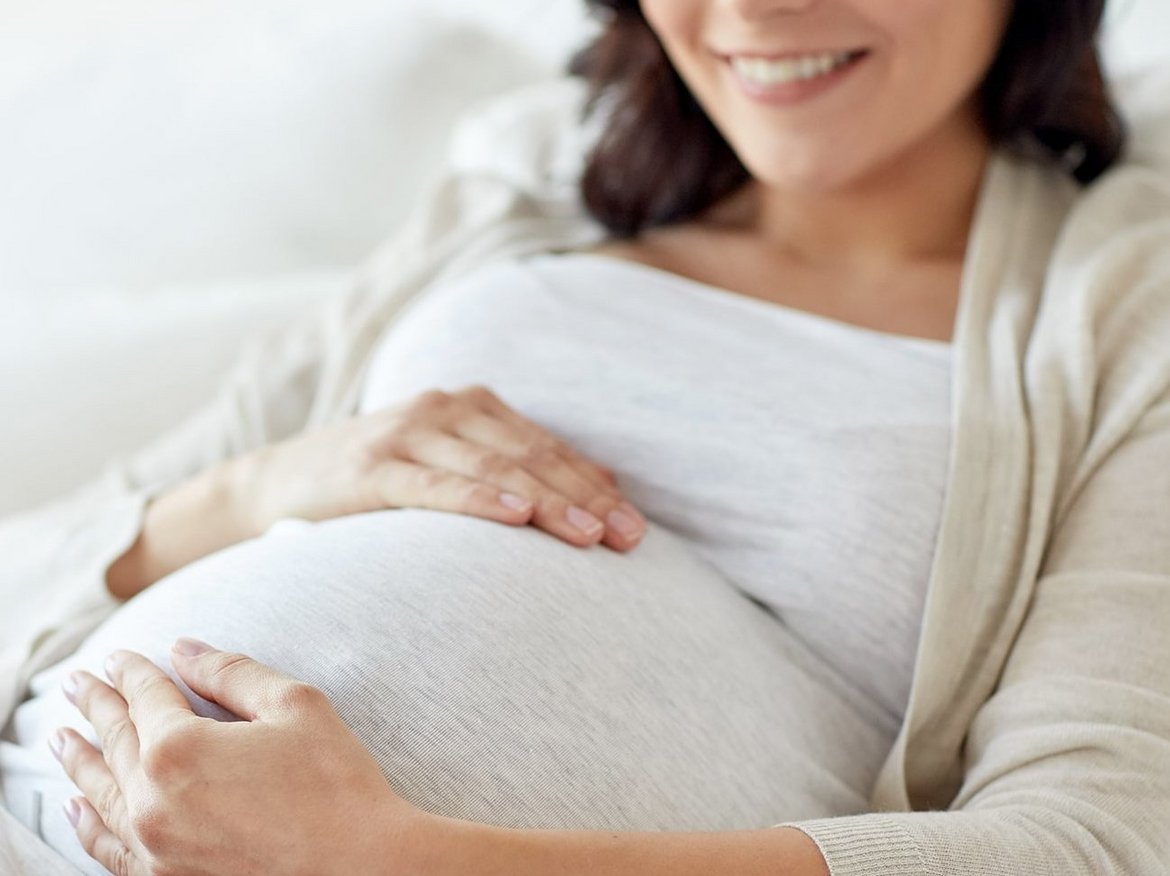 Frau sitzt und hat ihre Hände auf ihren Babybauch gelegt