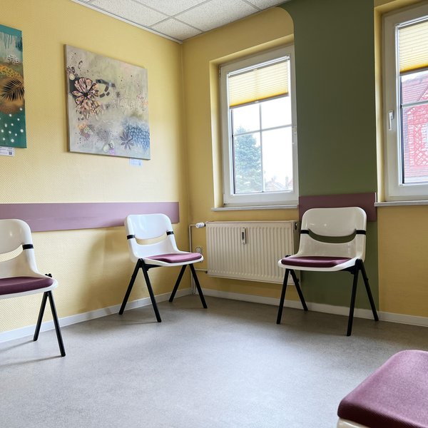 Helles Wartezimmer mit Stühlen und bunten Bildern an den Wänden.