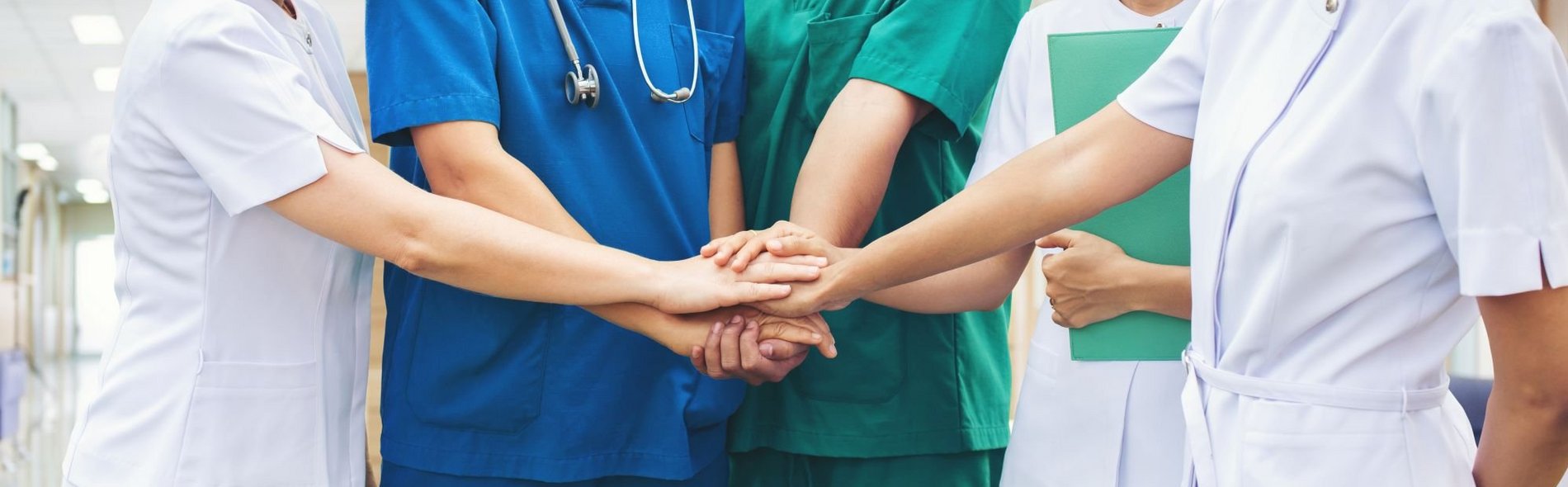 Mitarbeitende in einem Krankenhaus mit unterschiedlicher Dienstkleidung reichen sich die Hände