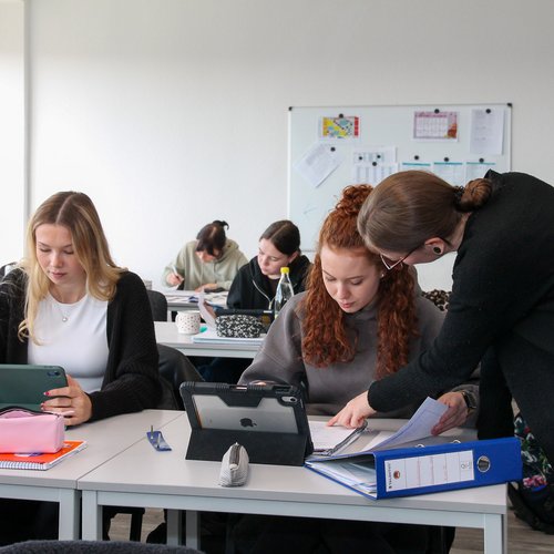 Blick in den Klassenraum, Lehrkraft gibt einer Auzubildenden Tipps zur Bearbeitung des Stoffes