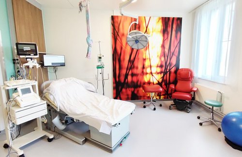 Kreißsaal mit Liege und rotem Sessel und Medizinball und einem roten Bild an der Wand