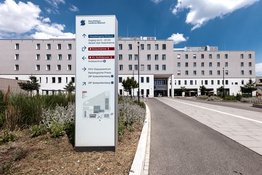 Das Foto zeigt das Zentralgebäude der Sana Kliniken Landkreis Biberach. Ein Hinweisschild zeigt den Weg zum Klinikum und zum Ärztehaus.