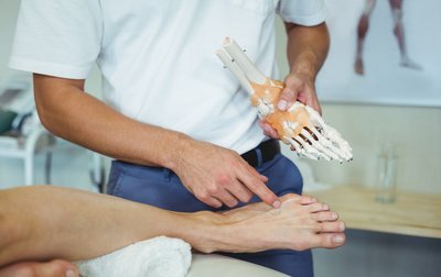Arzt untersuch Fuß eines Patienten und zeigt Fußmodell