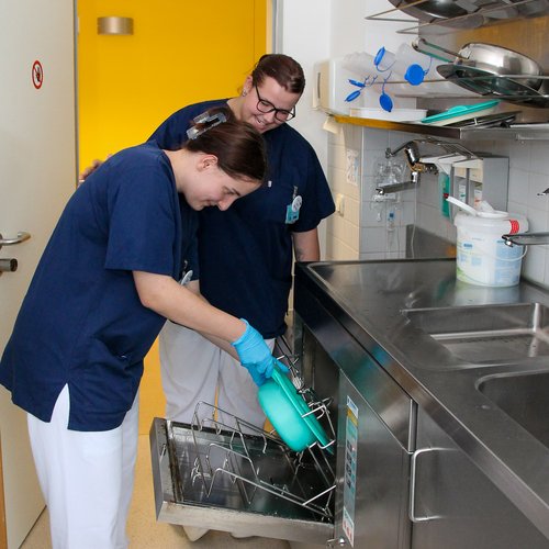 Ein Auszubildende zeigt einer Mitschülerin, wie der Waschautomat funktioniert.