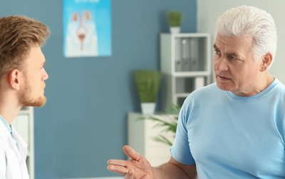 Ein Arzt in weißem Kittel im Gespräch mit einem Patienten.