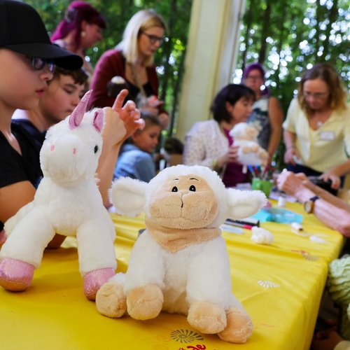 Auf einem Tisch liegen mehrere Plüschtiere. Um den Tisch sitzen mehrere Kinder und Erwachsene.
