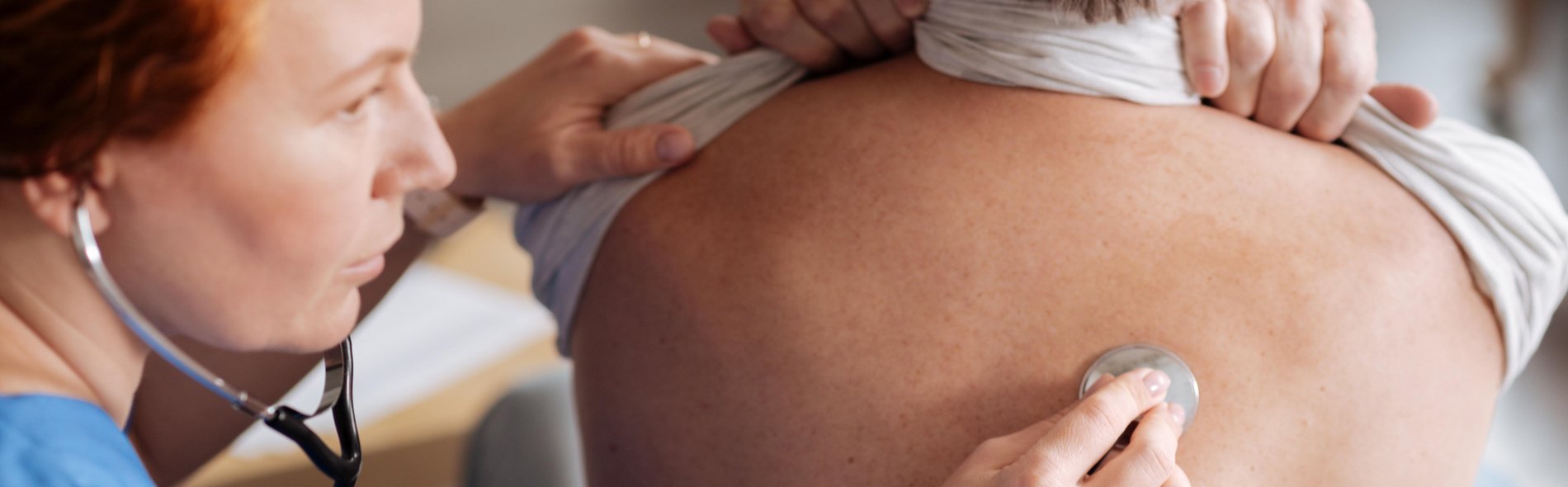 Ärztin hört mit einem Stethoskop am Rücken die Lunge eines Patienten ab