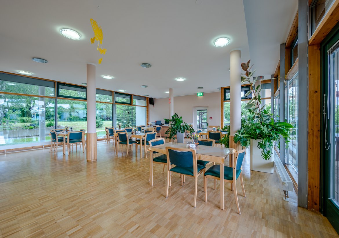 Heller Speisesaal im Pflegeheim mit großen Fenstern und einladender Einrichtung.  