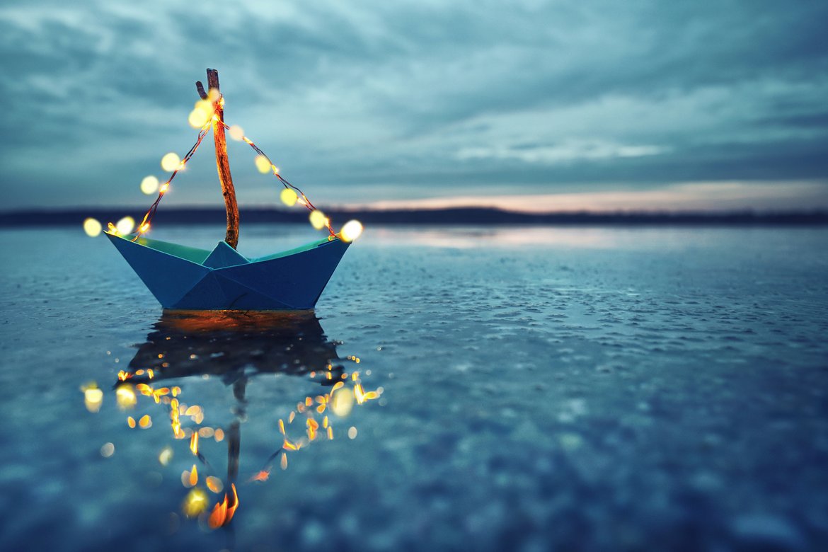 Ein Papierschiff mit einer kleinen Lichterkette treibt auf dem Wasser