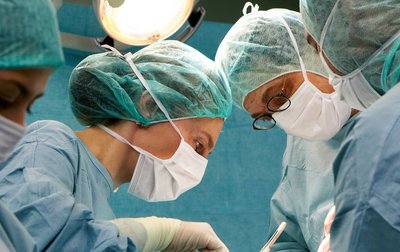 Ein OP-Team in OP-Kleidung und Masken, die während einer Operation unter hellen OP-Lampen konzentriert arbeiten.