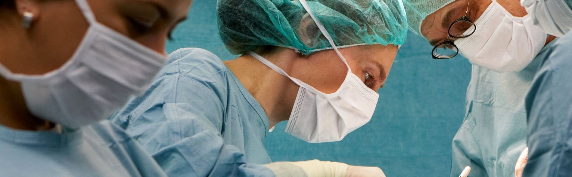Ein konzentriertes Operationsteam in blauen OP-Kitteln und Masken operiert in einem gut beleuchteten Raum. Die Szene vermittelt Präzision und Konzentration und unterstreicht Teamarbeit und Fachkompetenz.