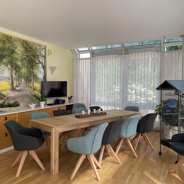 Heller Wintergarten mit einem großen Tisch und einer Vogelvoliere im Hospiz des Sana-Krankenhauses auf Rügen.