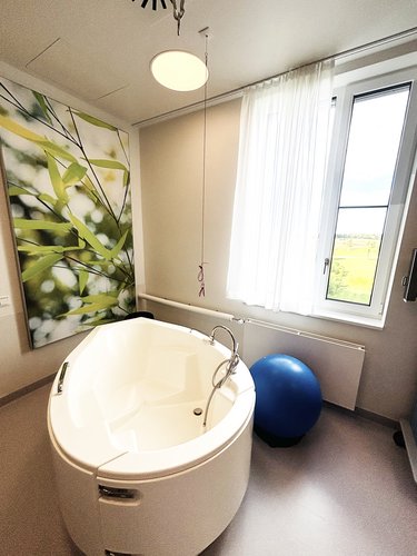 Ausschnitt von Kreißsaal 3 im Geburtszentrum Biberach, in grün gehalten, mit weißer Geburtswanne, blauem Pezziball sowie Ausblick ins Grüne 