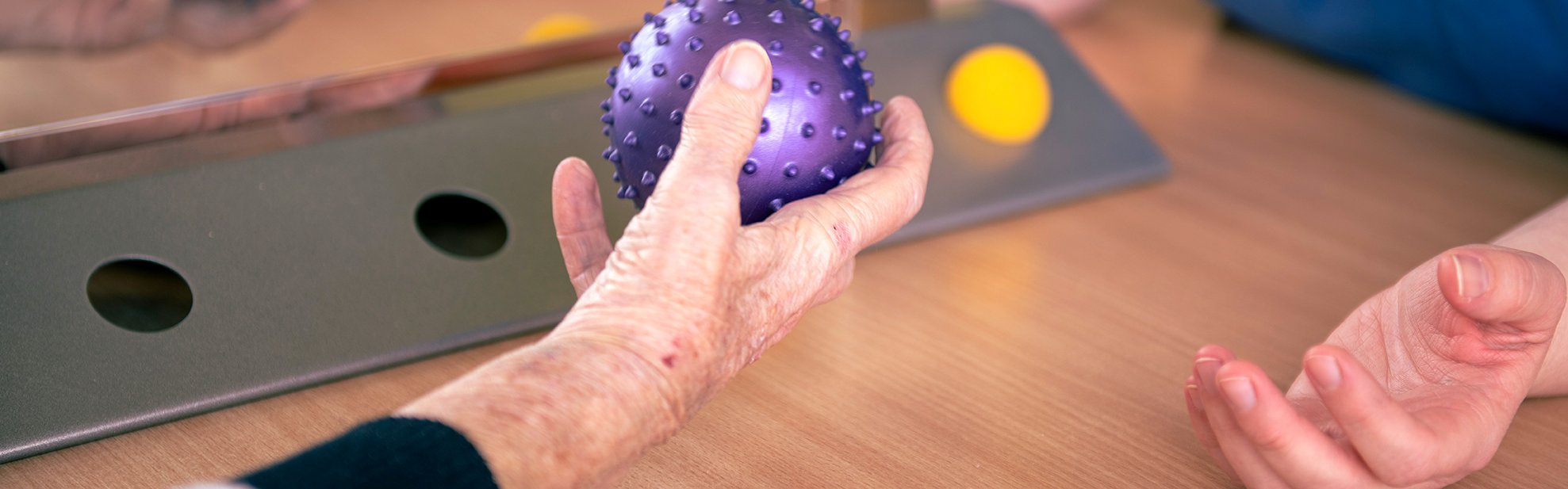 Bild zeigt ältere Patientin mit ihrer Ergotherapeutin beim Handtraining mittels Stachelball in der Ergotherapie am Sana Klinikum Borna