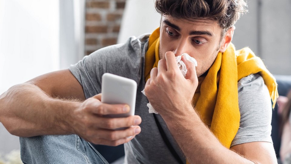 Mann mit verstopfter Nase und Smartphone