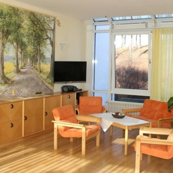 Heller, sonniger Aufenthaltsraum im Hospiz mit einer Sitzgruppe 