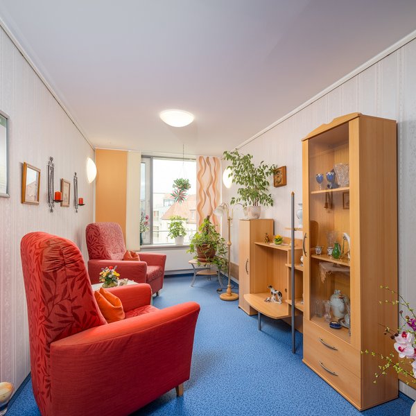 Gemütliche Sitznische mit roten Sesseln und Regalschrank in einem ruhigen Raum.