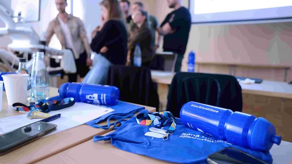 Blaue Trinkflaschen auf einem Tisch, im Hintergrund sind Teilnehmende der Summerschool im Gespräch