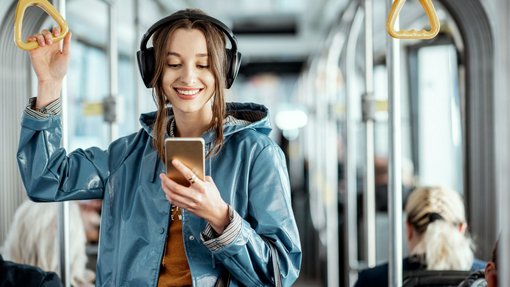 Foto von junger Frau in einem öffentlichen Verkehrsmittel, die freudig in ihr Smartphone schaut.